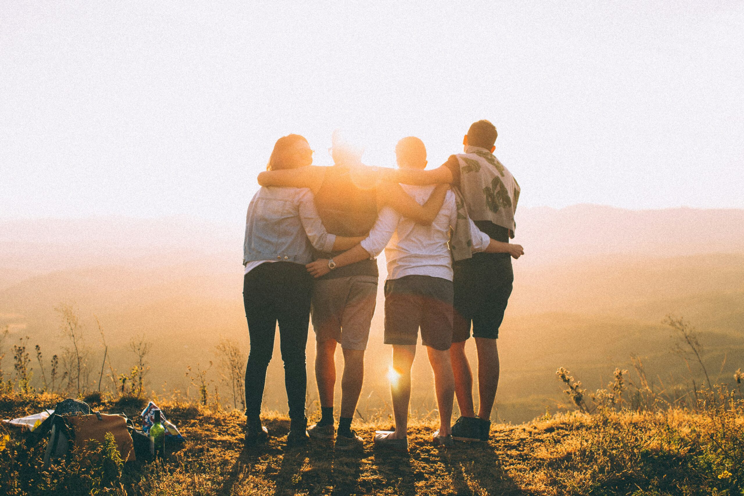four person hands wrap-around shoulders while looking at sunset