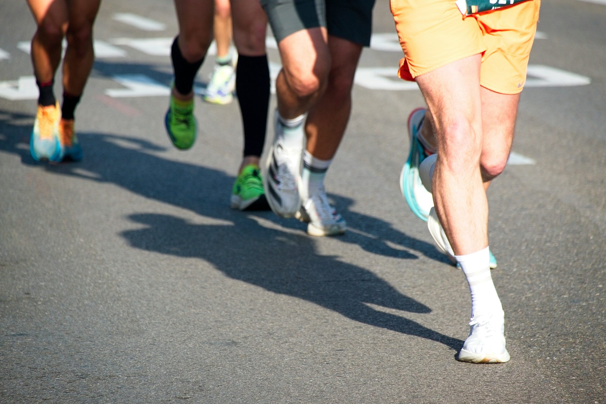 Runners' legs and feet in motion on asphalt with shadows